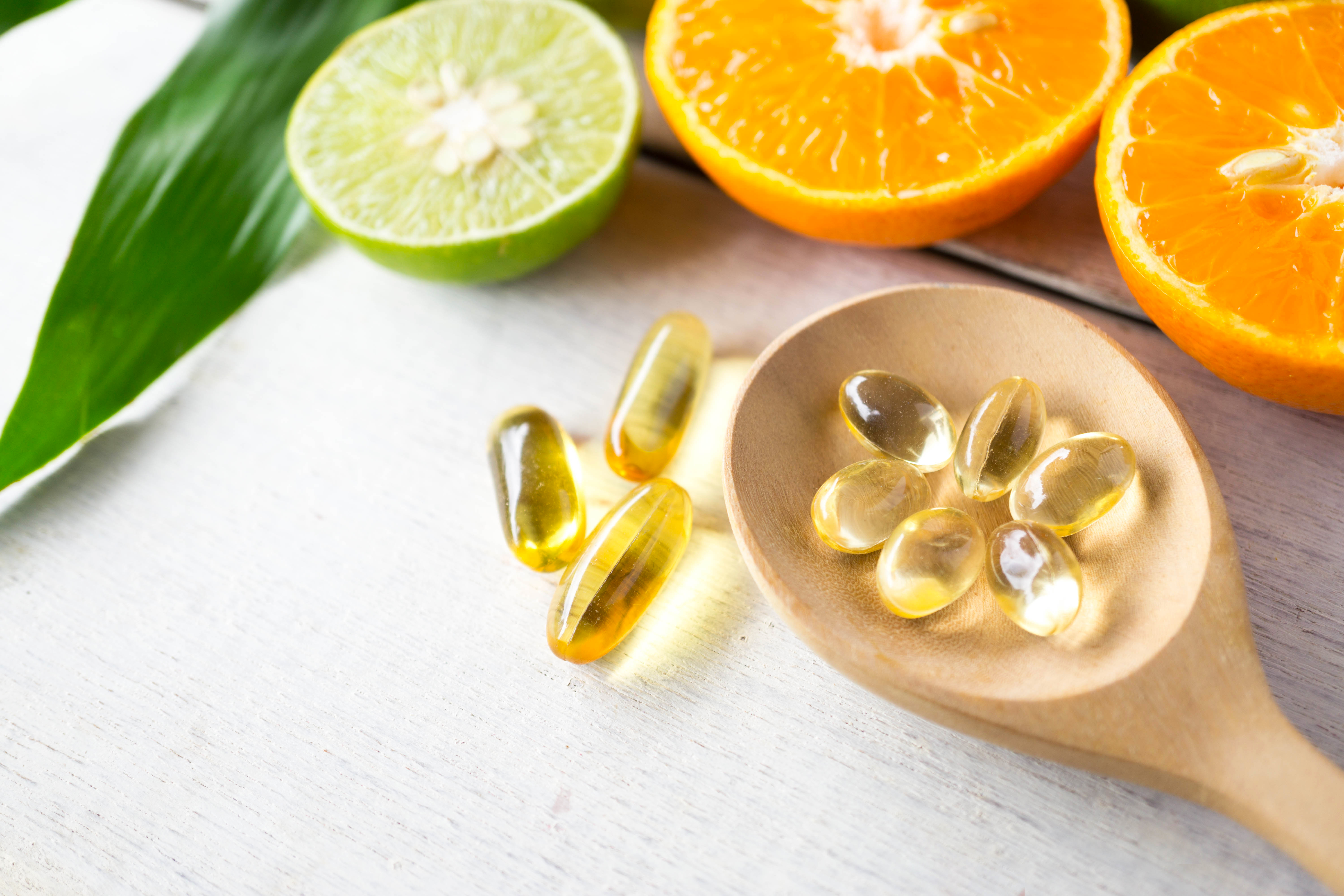 softgels on a wooden spoon next to oranges and lime